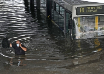 The driver of the bus speaks on his mobile phone as he wades through high water after evacuating the passengers from the bus stuck in a flooded underpass in southern Athens, Thursday, Oct. 14, 2021. Storms have been battering the Greek capital and other parts of southern Greece, causing traffic disruption and some road closures. (AP Photo/Thanassis Stavrakis)