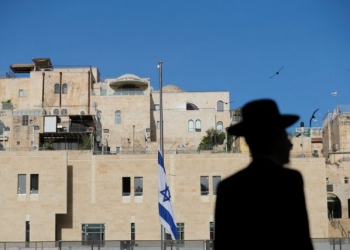 An ultra-Orthodox Jewish man is silhouetted near the Israeli national flag, which was lowered to half-mast as the country observes a day of mourning after dozens were crushed to death in a stampede at a religious festival on the slopes of Israel’s Mount Meron, at the Western Wall in Jerusalem's Old City May 2, 2021. REUTERS/Ammar Awad