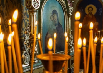 Blurred wax burning candles in an orthodox church on the icon background.